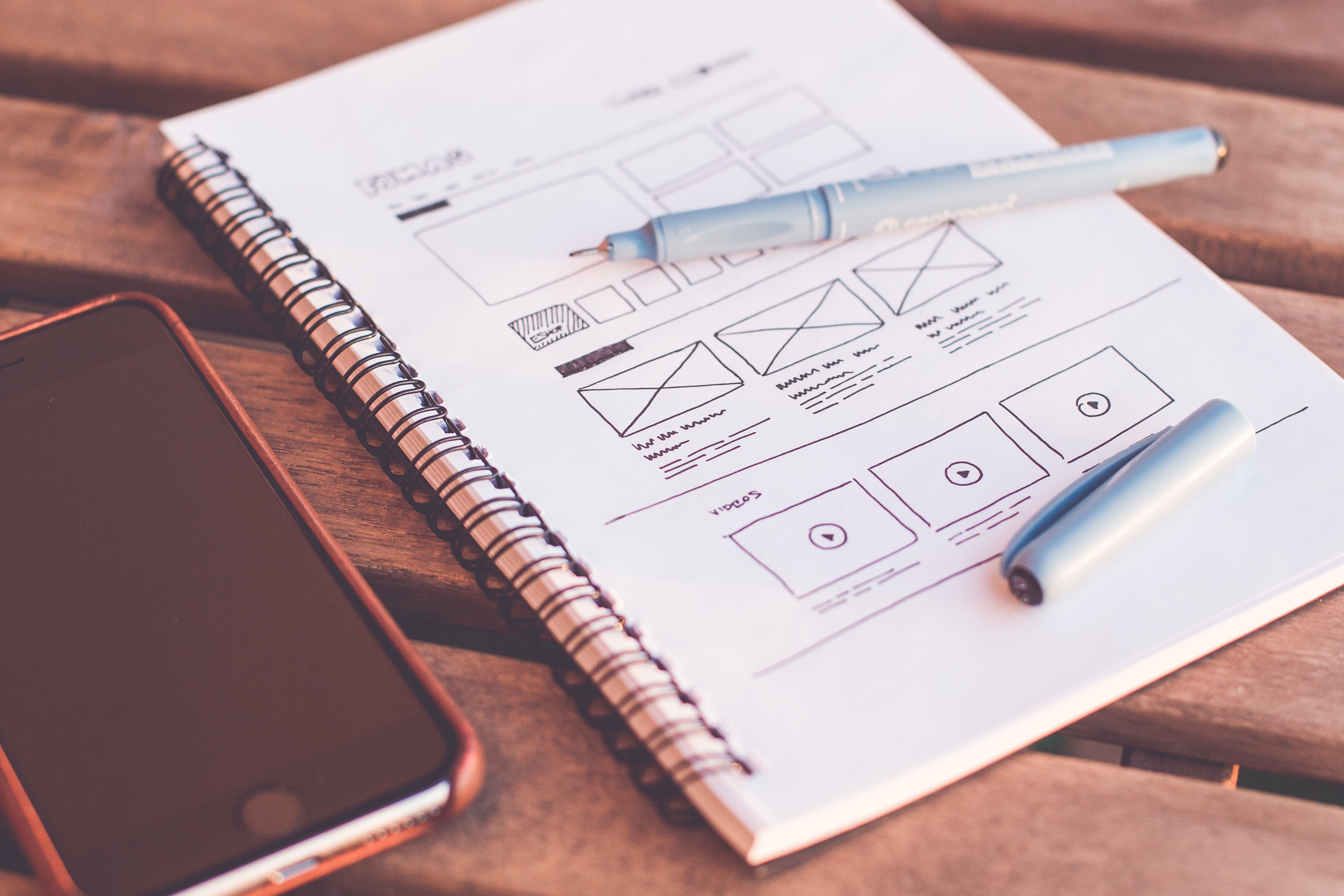 phone beside notebook showing wireframe designs